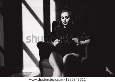 Black and white picture of pregnant woman sitting on the chair. Sun rays shine on a woman