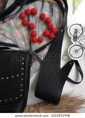 Black leather female sash belt, a fragment of a black bag and red beads from threads on a white table