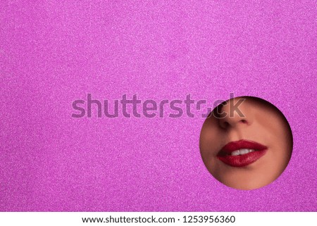 View of bright lips through hole in shimmer violet paper background. Make up artist, beauty concept. Ready to new year party. Cosmetics sale. Beauty salon advertising banner with copy space.