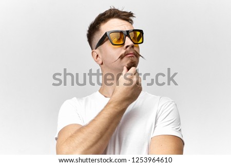 Thoughts, ideas and human facial expressions. Isolated shot of handsome guy with trendy hairstyle and handlebar mustache, having pensive thoughtful look, stroking his goatee beard in studio