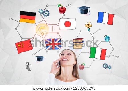 Cheerful young woman talking on smartphone looking at colorful international education sketch drawn on white wall with geometric pattern