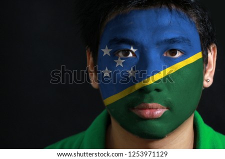 Portrait of a man with the flag of the Solomon Islands painted on his face on black background. The concept of sport or nationalism.