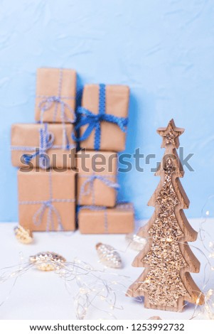 Decorative fir tree and stack or pile of wrapped boxes with presents  on white textured background against blue wall. Selective focus.  Holiday shopping concept. Vertical image. 
