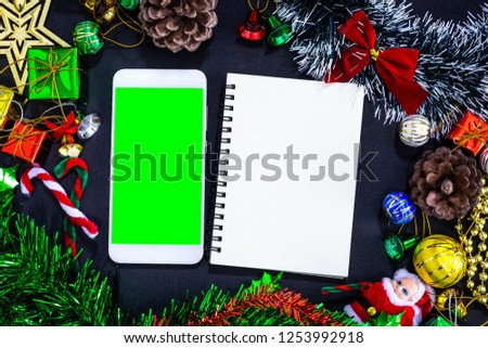 Top view image of Christmas festive decorations with empty smartphone,notebook and pencil on black paper background, New Year concept.