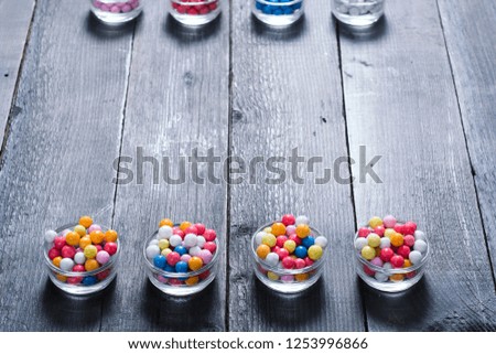 dragees, sugar coated pills at glass dish, on black wood table background