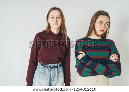 Two sisters twins beautiful girls hipsters in casual clothing antipodes smiling and sad on grey background isolated