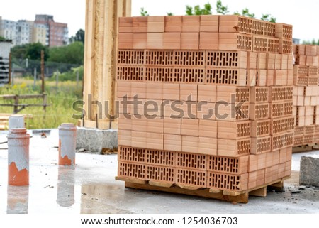 Construction of new house concept. Vertical photo red rectangular brick tray lay in stack on floor foundation outside