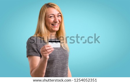 Middle-age blonde woman holding a credit card on colorful background