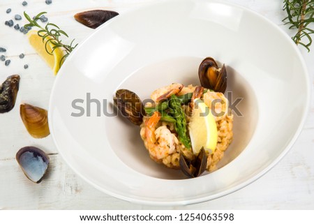 An overhead photo of a seafood risotto on teal textures, with a fork and a spoon, a glass of white wine, and a place for text
