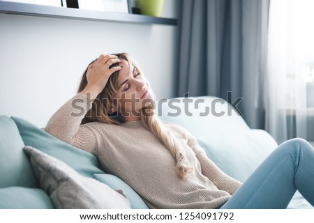 Sad woman sitting on sofa at home, thinking about important things Royalty-Free Stock Photo #1254091792