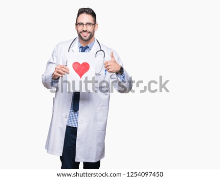 Handsome young doctor man holding paper with red heart over isolated background happy with big smile doing ok sign, thumb up with fingers, excellent sign