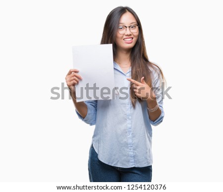 Young asian woman holding blank paper over isolated background very happy pointing with hand and finger