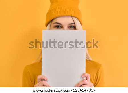Indoor closeup monochrome portrait of of cheerful woman covers face with white book, has joyful expression, blank copy space for your advertising or promotional text, isolated on yellow background.