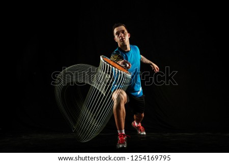Young man playing badminton over neon black studio background. Fit male athlete isolated on dark with led light trail . badminton player in action, motion, movement. attack and defense concept