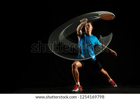 Young man playing badminton over black studio background. Fit male athlete isolated on dark with led light trail . badminton player in action, motion, movement. attack and defense concept