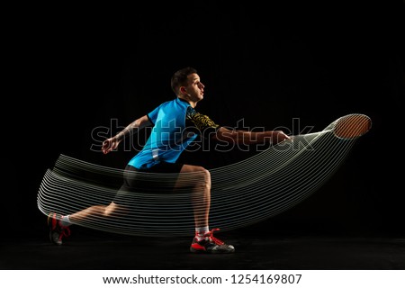 Young man playing badminton over black studio background. Fit male athlete isolated on dark with led light trail . badminton player in action, motion, movement. attack and defense concept