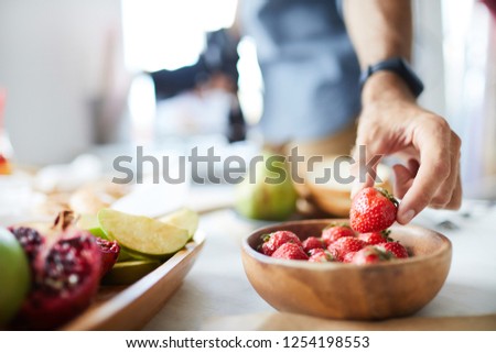 Closeup of unrecognizable photographer holding single strawberry while doing food-photography in studio, copy space