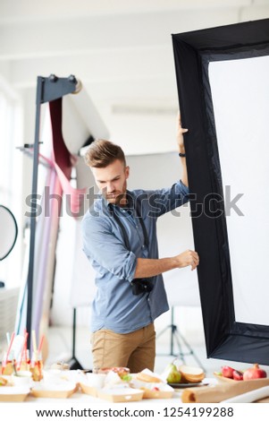 Portrait of handsome photographer adjusting light equipment in photo studio