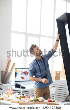 Portrait of handsome photographer adjusting light equipment in photo studio, copy space
