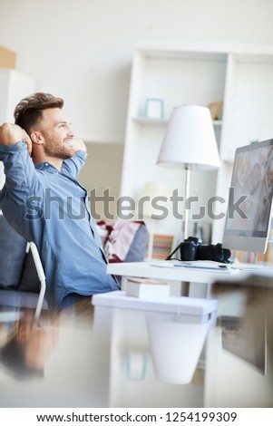 Side view portrait of professional photographer leaning back in chair while editing photos at workplace