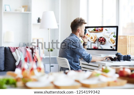 Side view portrait of young photographer editing photos of food sitting at desk at home, copy space
