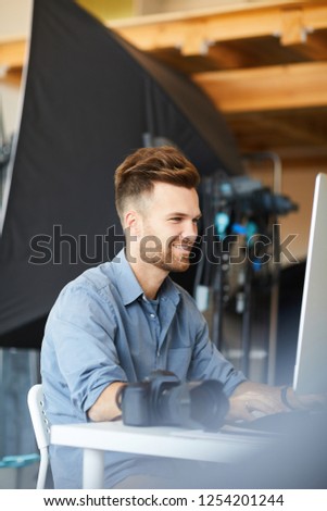 Side view portrait of handsome male photographer working in studio using computer against lighting equipment