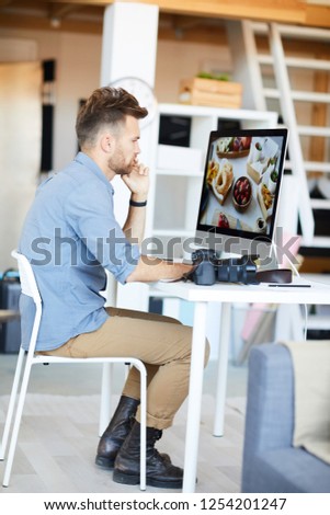 Full length side view portrait of male photographer editing photos using computer in studio