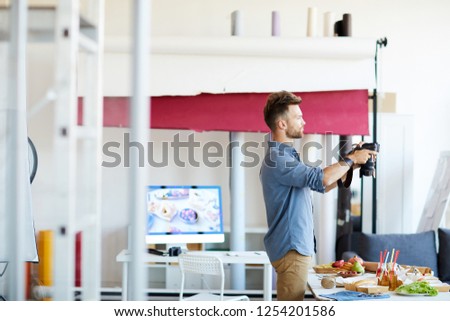 Side view portrait of young photographer taking pictures of food in studio, copy space