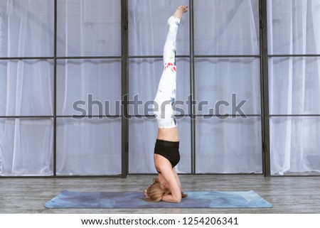 Young woman practicing yoga indoors. Yogi headstand in pose Sirshasana in yoga mat