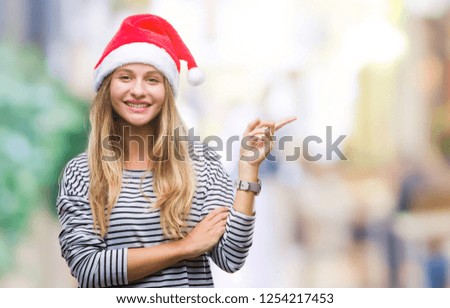 Young beautiful blonde woman wearing christmas hat over isolated background with a big smile on face, pointing with hand and finger to the side looking at the camera.
