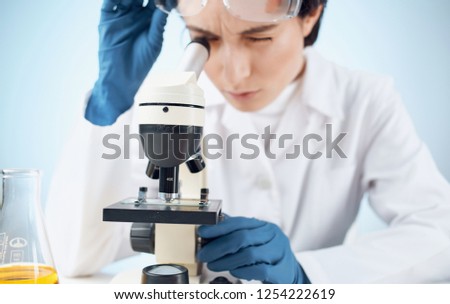 A lab technician looks through a microscope while raising his glasses                       