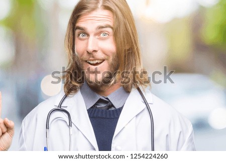Young handsome doctor man with long hair over isolated background pointing finger up with successful idea. Exited and happy. Number one.