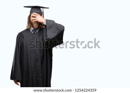 Young handsome graduated man with long hair over isolated background peeking in shock covering face and eyes with hand, looking through fingers with embarrassed expression.
