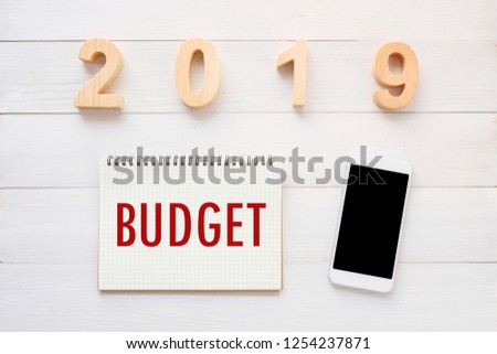 2019 budget word on notebook paper background and smart phone on white wood background, financial concept, business strategy