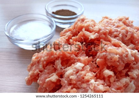 Homemade raw ground minced pork and beef meat ready for cooking with salt and pepper in bowls on wooden table background. Close up photography