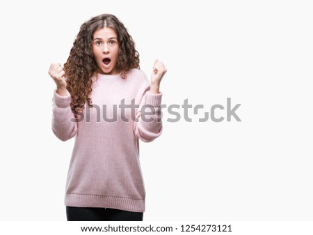 Beautiful brunette curly hair young girl wearing pink winter sweater over isolated background celebrating surprised and amazed for success with arms raised and open eyes. Winner concept.