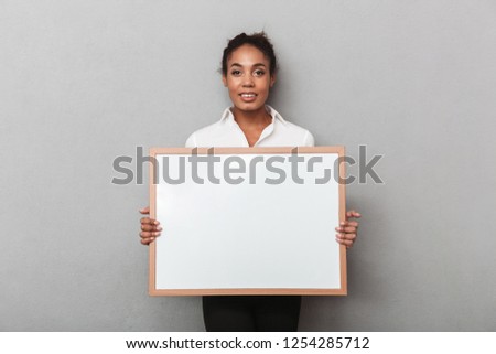 Attractive young african business woman wearing shirt standing isolated over gray background, holding blank board