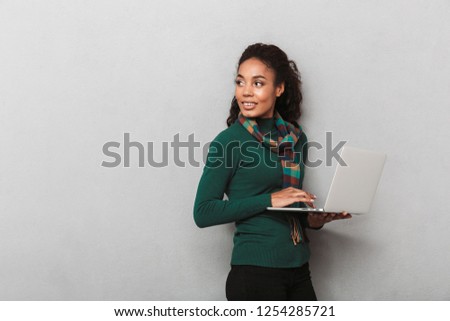 Cheerful african woman wearing scarf standing isolated over gray background, holding laptop computer