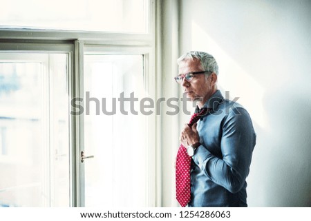 Mature businessman on a business trip standing in a hotel room, getting dressed.