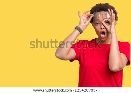 Beautiful young african american woman wearing glasses over isolated background doing ok gesture shocked with surprised face, eye looking through fingers. Unbelieving expression.