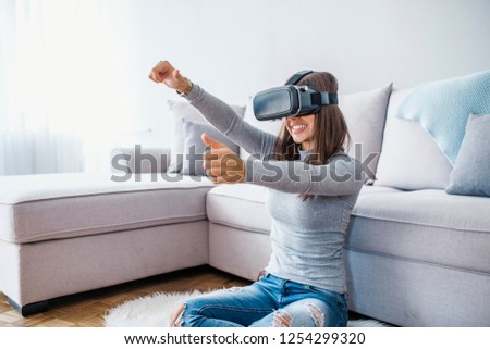 Woman with virtual reality glasses. Smiling young woman using VR headset at home on couch. Woman enjoying virtual reality at home. Beautiful Woman wearing VR Virtual Reality Headset with Interface.