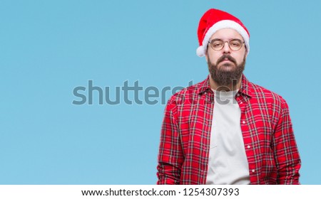 Young caucasian man wearing christmas hat over isolated background with serious expression on face. Simple and natural looking at the camera.