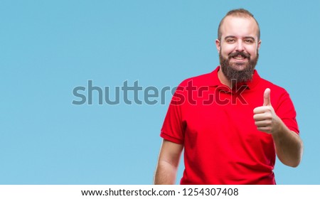Young caucasian hipster man wearing red shirt over isolated background doing happy thumbs up gesture with hand. Approving expression looking at the camera with showing success.