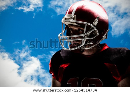 American football player standing in helmet against view of beautiful sky and clouds