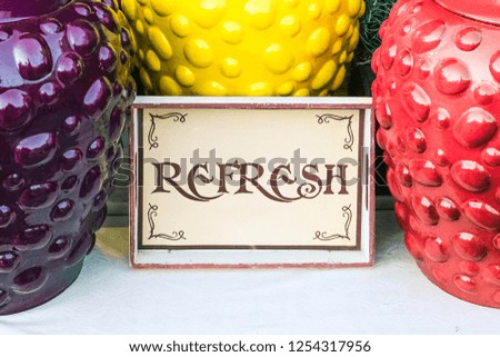 Closeup view paper plate Refresh sign surrounded by big earthen jars in the shape of colorful berries. Fair decorative ceramic vessels for drink and beverages