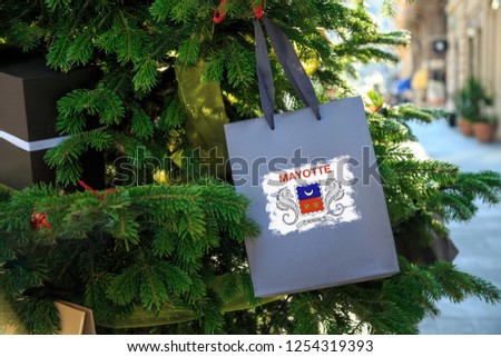 Mayotte flag printed on a Christmas shopping bag. Close up of a shopping bag as a decoration on a Xmas tree on a street. New Year or Christmas shopping, local market sale and deals concept. 