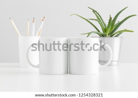 Two mugs mockup with workspace accessories and a succulent plant on a white table. Royalty-Free Stock Photo #1254328321