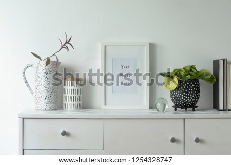 Scandinavian stylish cupboard with mock up poster frame, design vase, accessories, books and beauty plant. White background wall.