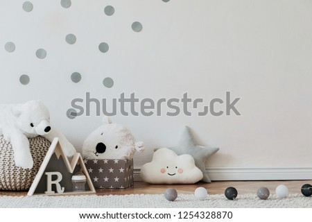 Stylish scandinavian newborn baby interior with mock up photo poster frame on the pattern wall, boxes, teddy bears and toys. White walls, wooden accessories and toys. Copy space.