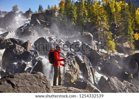 Happy man with backpack enjoying amazing waterfall Travel Lifestyle and success concept vacations into the wild nature